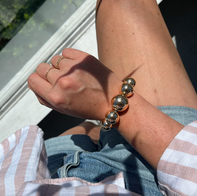Close-up of a person's wrist wearing a gold bracelet with sunlight casting shadows.