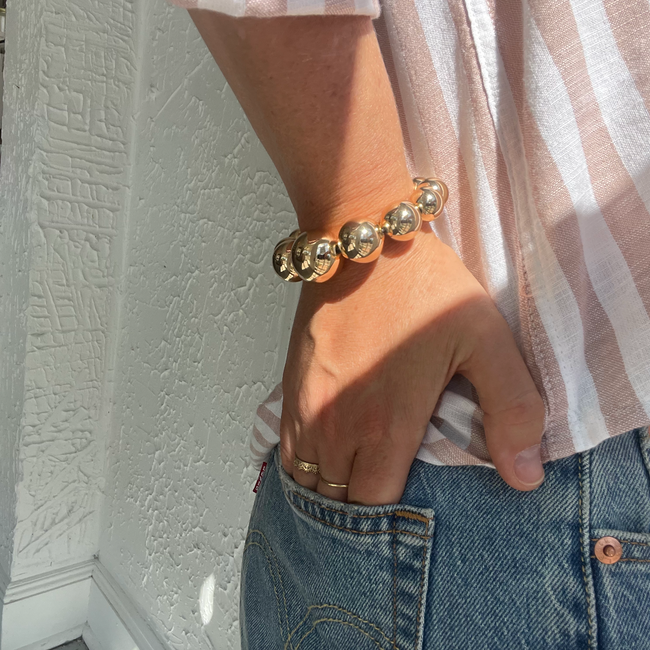 Person wearing a gold bracelet and ring, with a neutral background