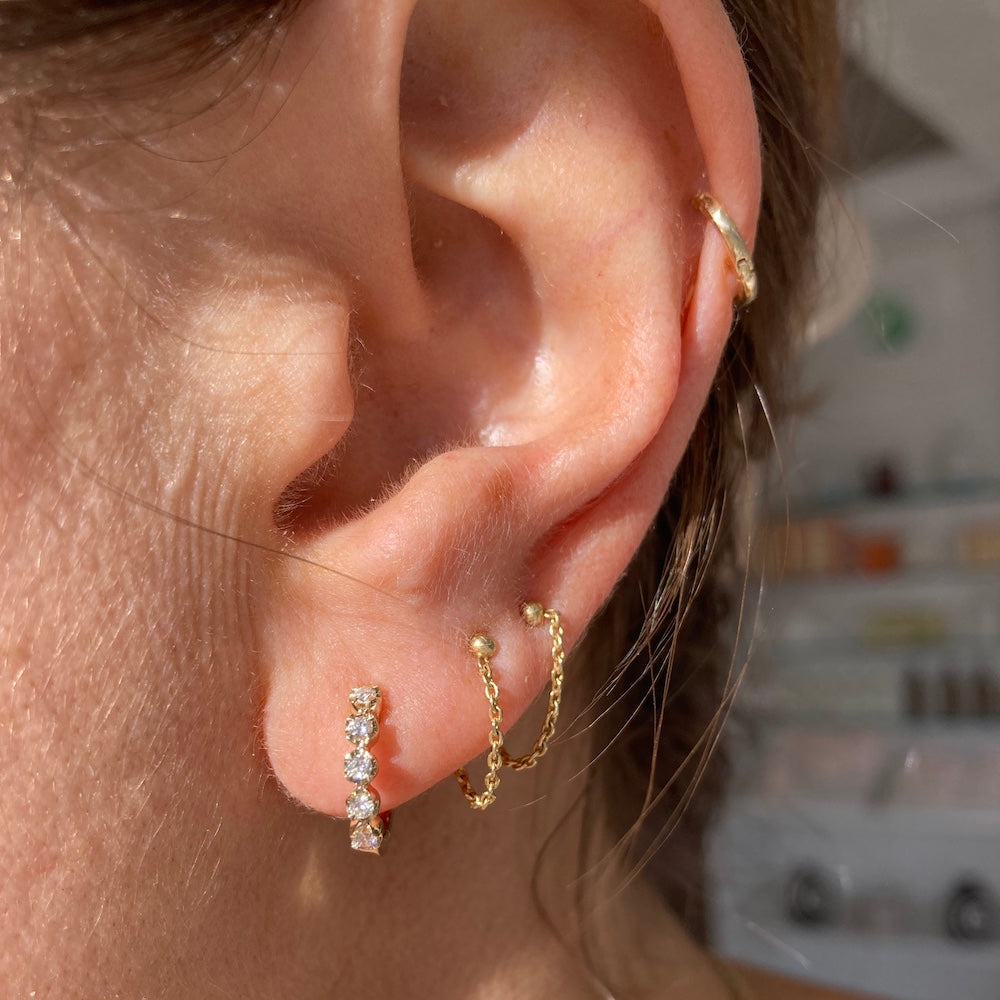 The secret garden huggie hoops are pictured here with our best selling chained together studs. In the cartilage is our 9mm charmed huggie hoop.