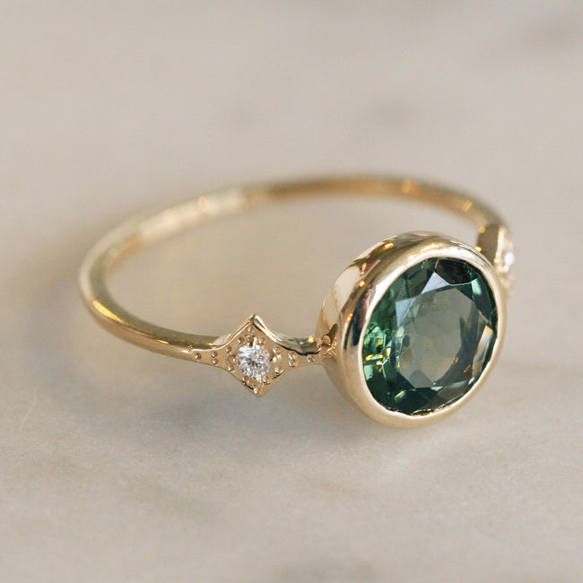Katie Diamond's Savannah Ring in Green Tourmaline. This Engagement Ring has a bezel set center stone and two side diamonds set in a diamond shape textured setting.