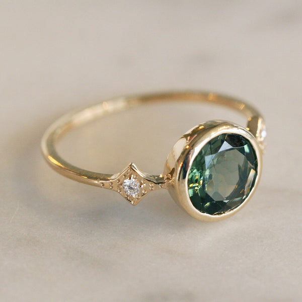 Katie Diamond's Savannah Ring in Green Tourmaline. This Engagement Ring has a bezel set center stone and two side diamonds set in a diamond shape textured setting.